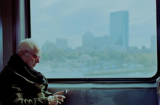 A man looking down at his phone as he rides the train. The city looms in the background.