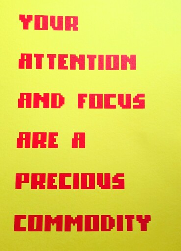 Bright red, pixelated text on a yellow field that reads, "YOUR ATTENTION AND FOCUS ARE A PRECIOUS COMMODITY"